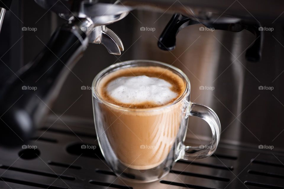 Freshly brewed cup of espresso with foam resting on an espresso machine 