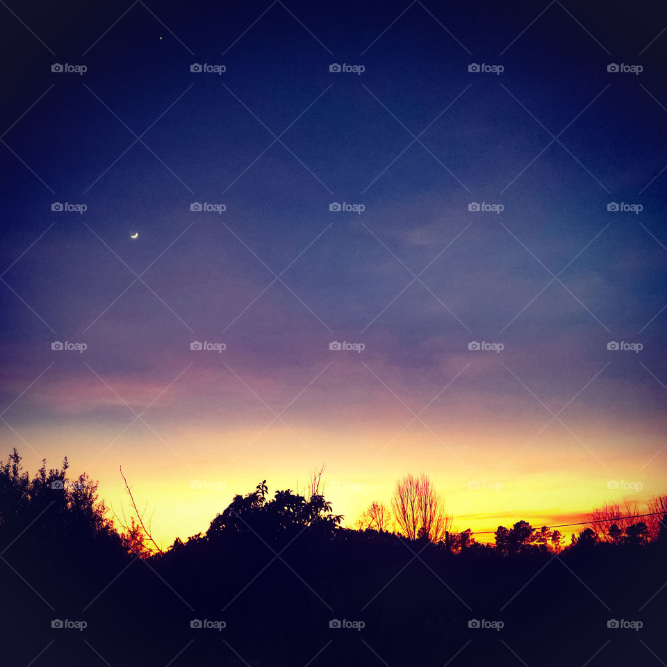 Just after the sun has gone down there is a bright orangey yellow strip along the horizon, higher in the sky it is dark with a crescent moon becoming visible