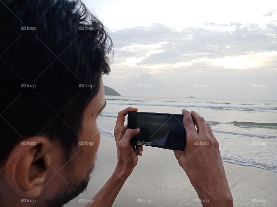 Yang mane holding mobile phone for capchar the beautiful sunset in beach