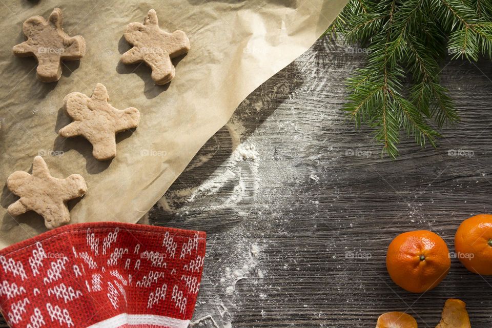 Christmas, gingerbread cookies on a wooden table sprinkled with flour, with tangerines and a green Christmas tree.