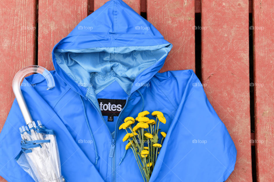 Flat lay of a blue raincoat with a bouquet of flowers and an umbrella