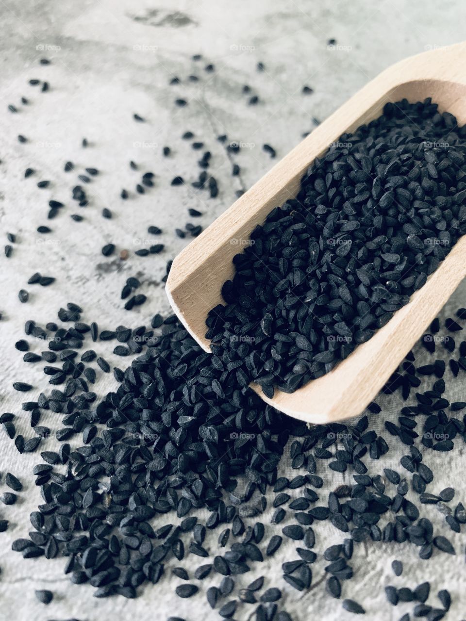 Overhead view of black seed spilling out of a wooden scoop on stone surface 