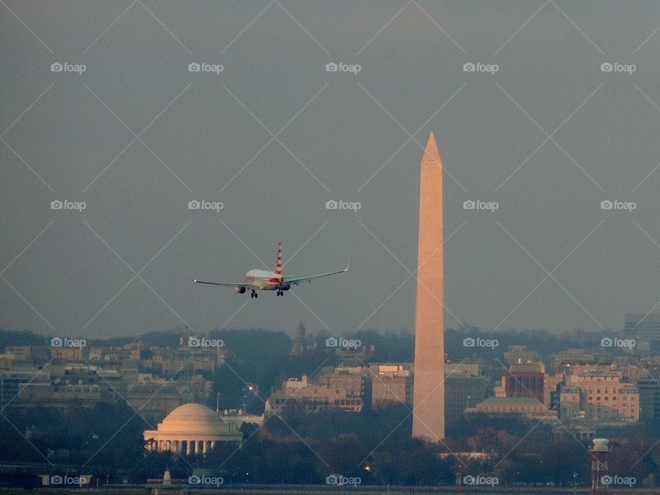 DC. An American Airlines plane preparing to land glides past some of Washington's iconic landmarks at sunset, seen from the Woodrow Wilson Bridge