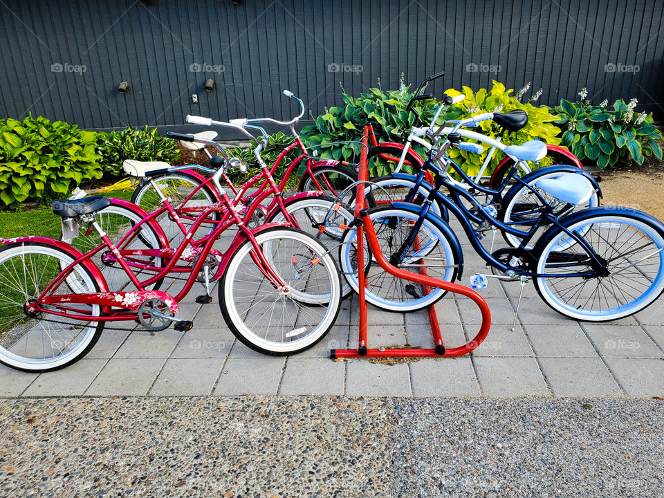 Red and blue bicycles are tied to a bicycle rack in a urban environment