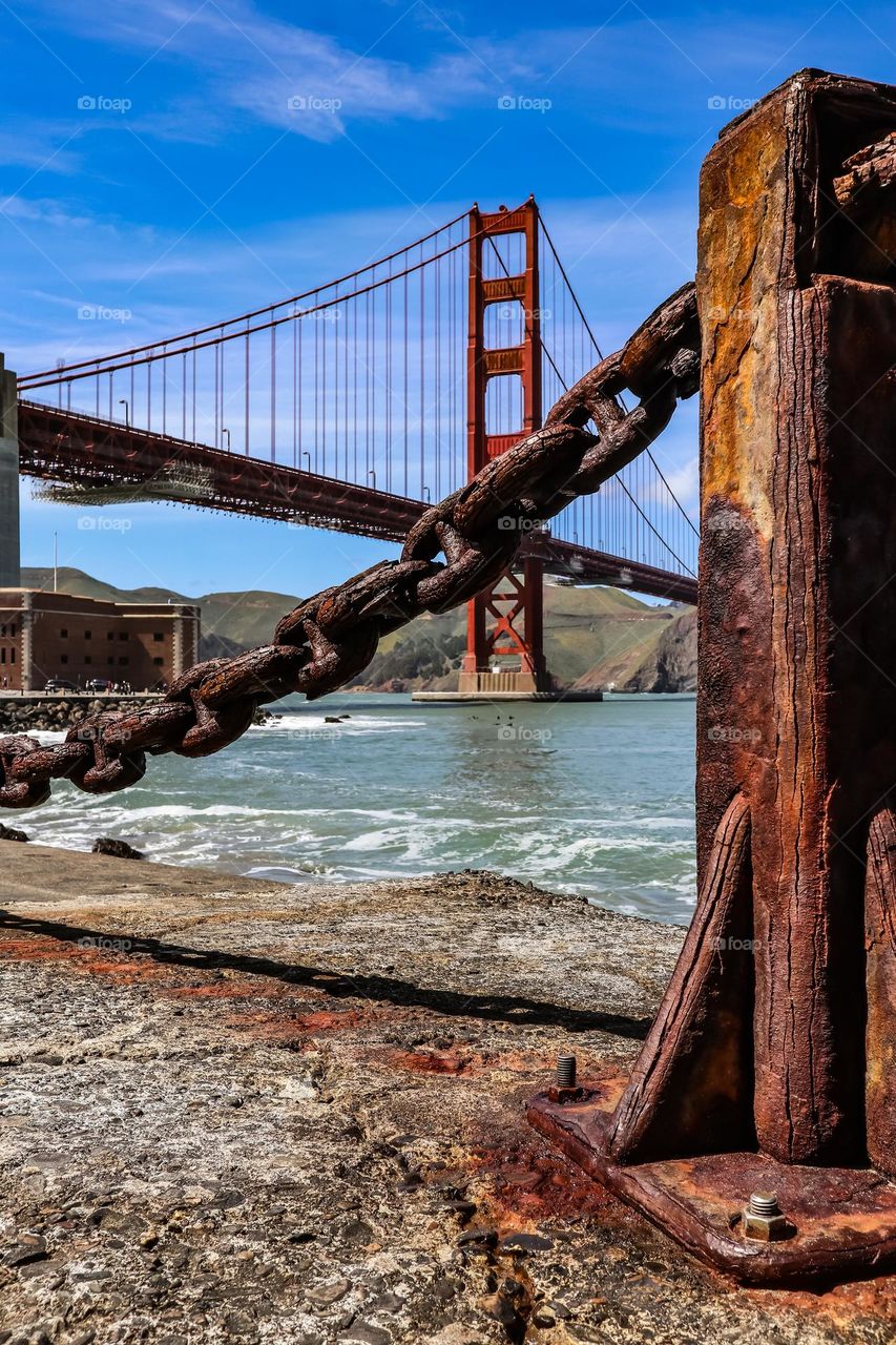 Looking at the Golden Gate Bridge through the rustic iron chain link guard rails with all their beautiful aged patina on a beautiful sunny day at Fort Point