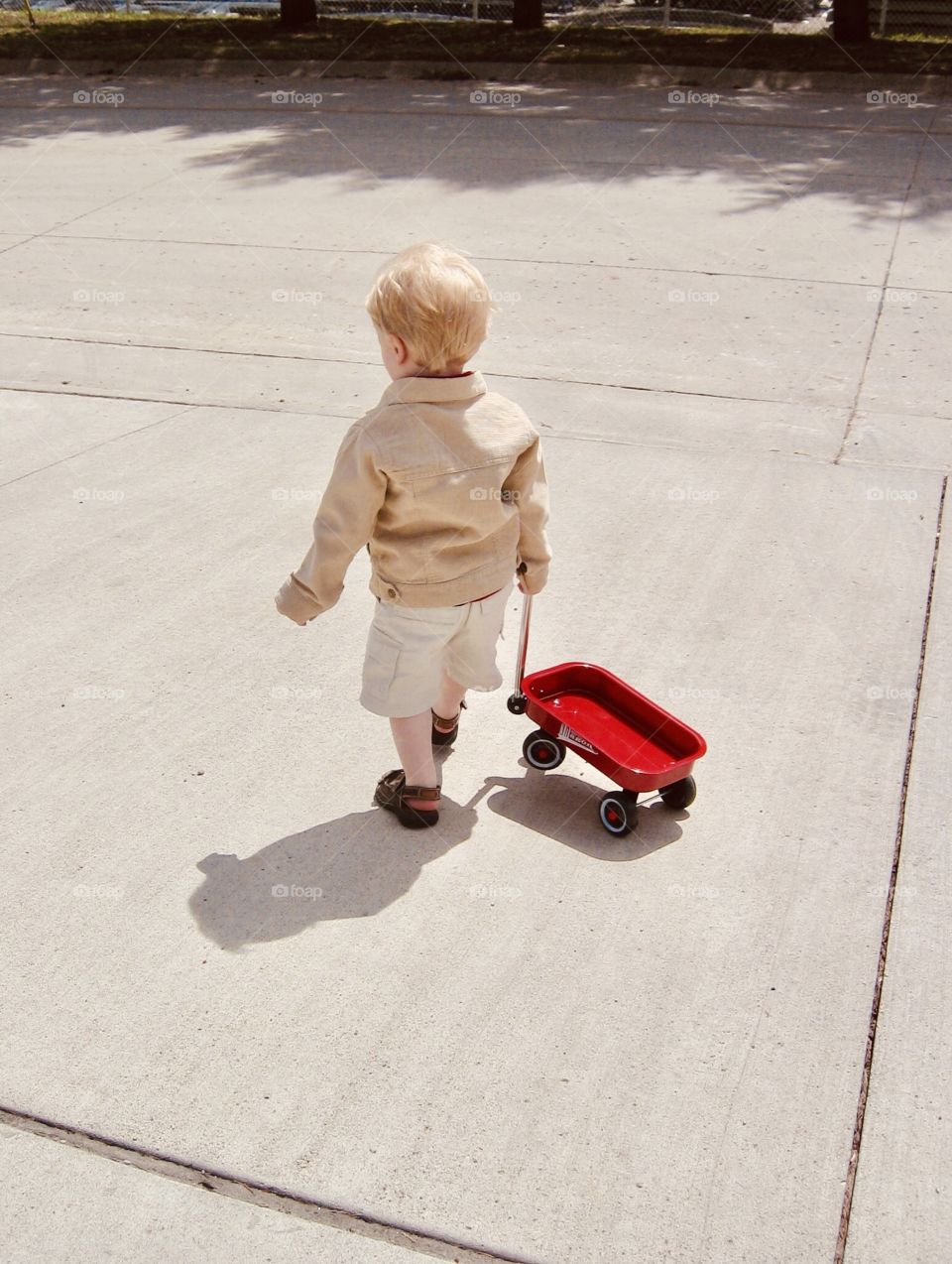 Young boy in light brown denim jacket and sandals pulling little red wagon makes this photo quite darling! 