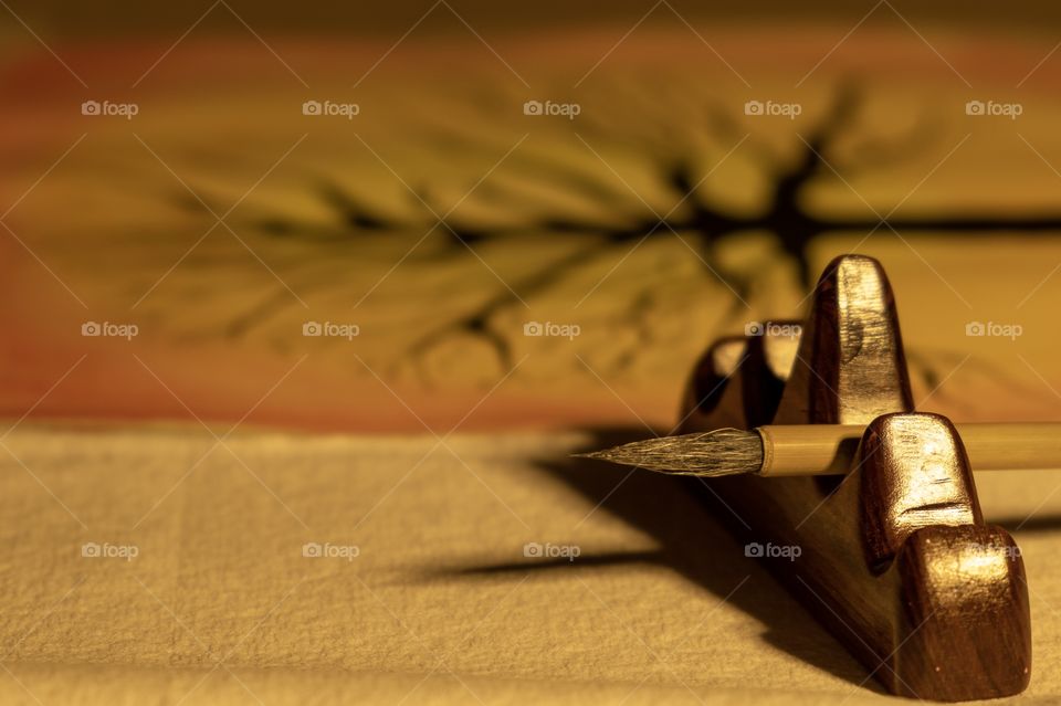 Artwork of a tree using watercolor and India ink. Closeup of a Chinese calligraphy brush resting on a hardwood holder. 