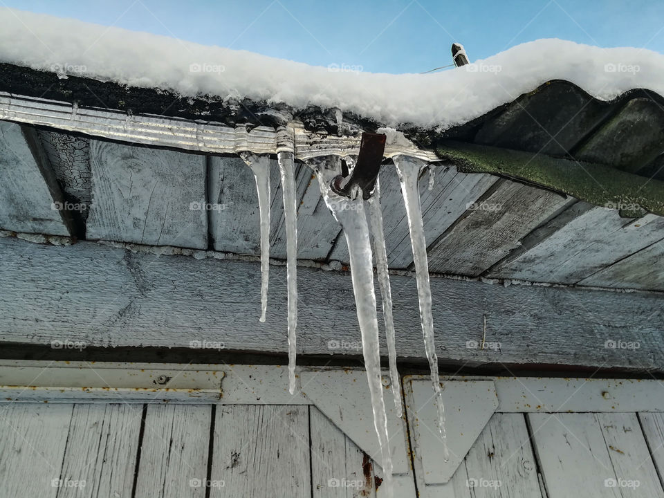Big icicles hanging from rooftop; cold winter