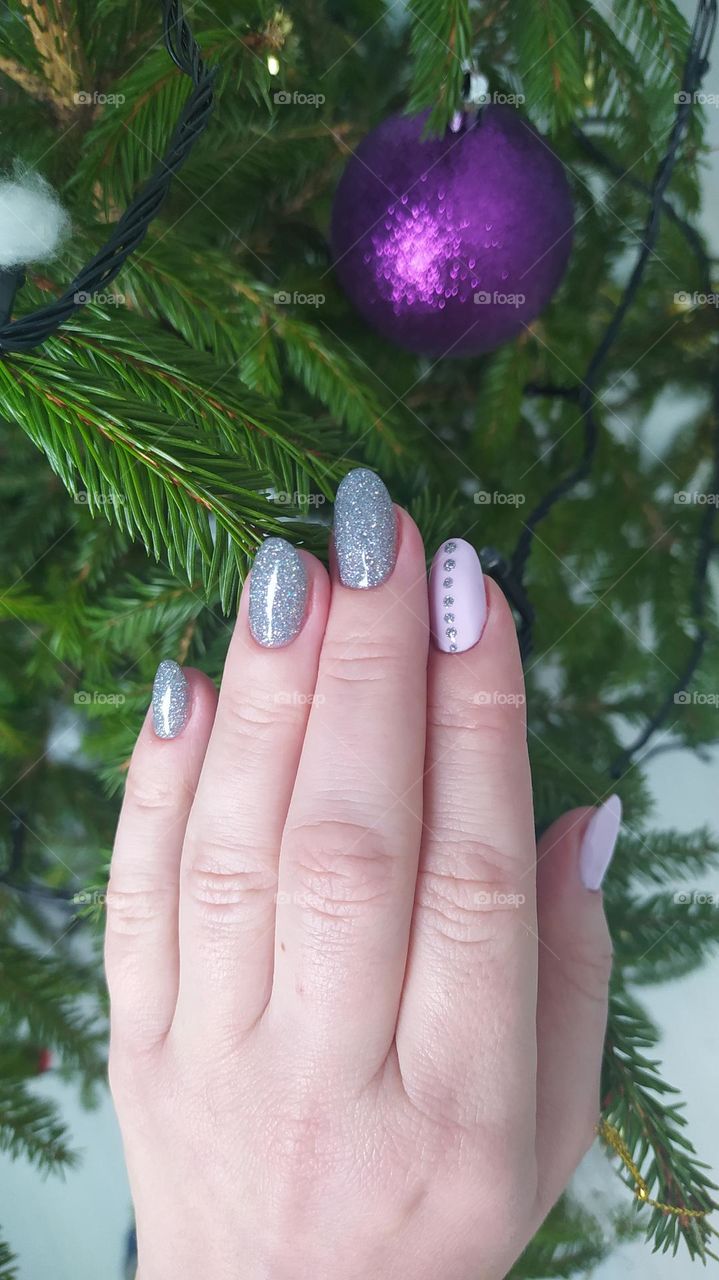 A female hand on the background of a New Year's, green Christmas tree with garlands and balls.