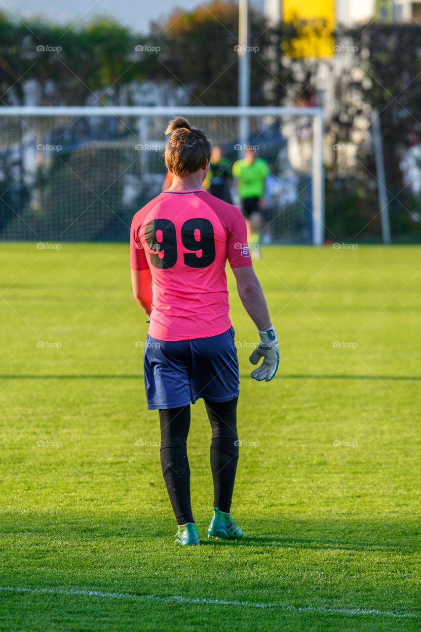 Rear view of goalkeeper wering jersey with number 99 standing in front of goal at an official football match