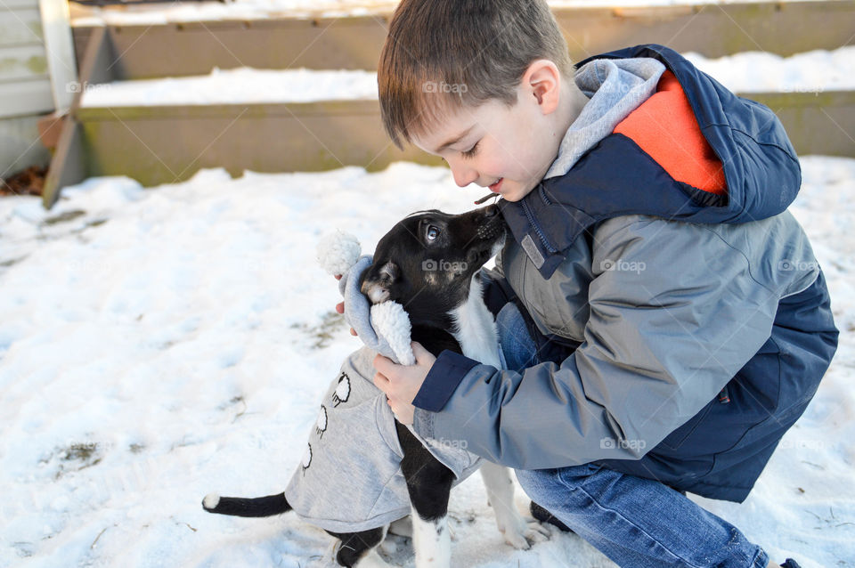 Young boy hugging his new puppy in the snow