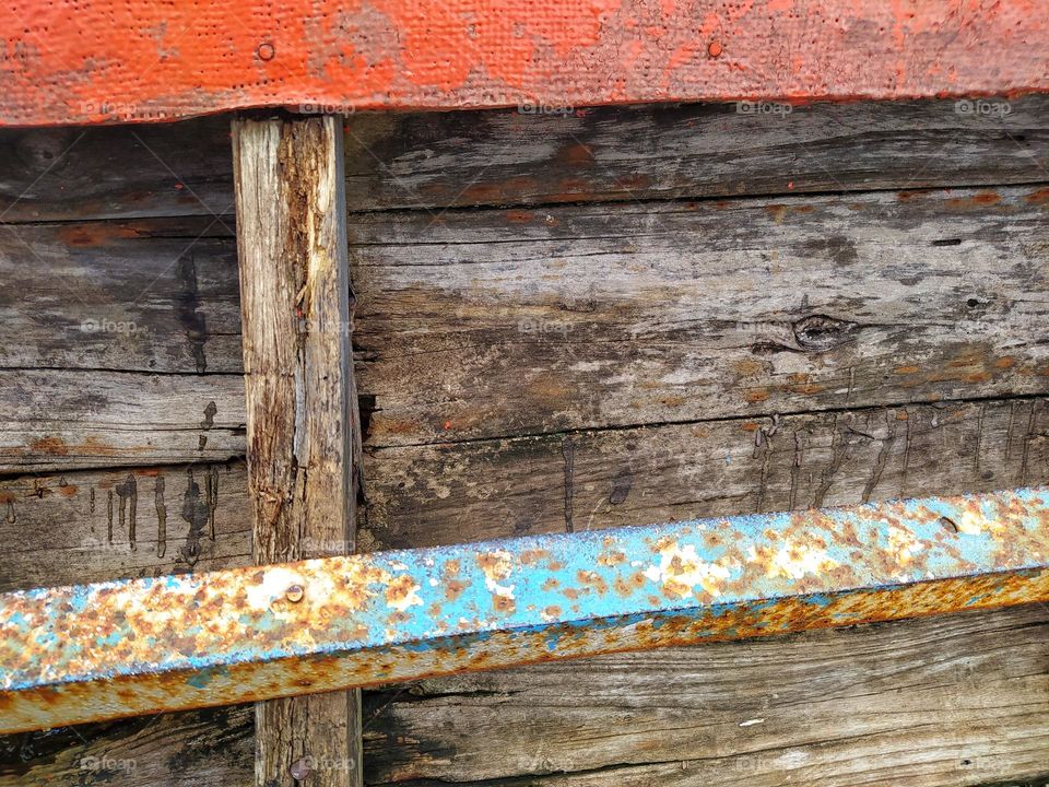 An interior side of a traditional fishing boat with wooden planks stacked horizontally and reinforced with long metal rods, then nailed