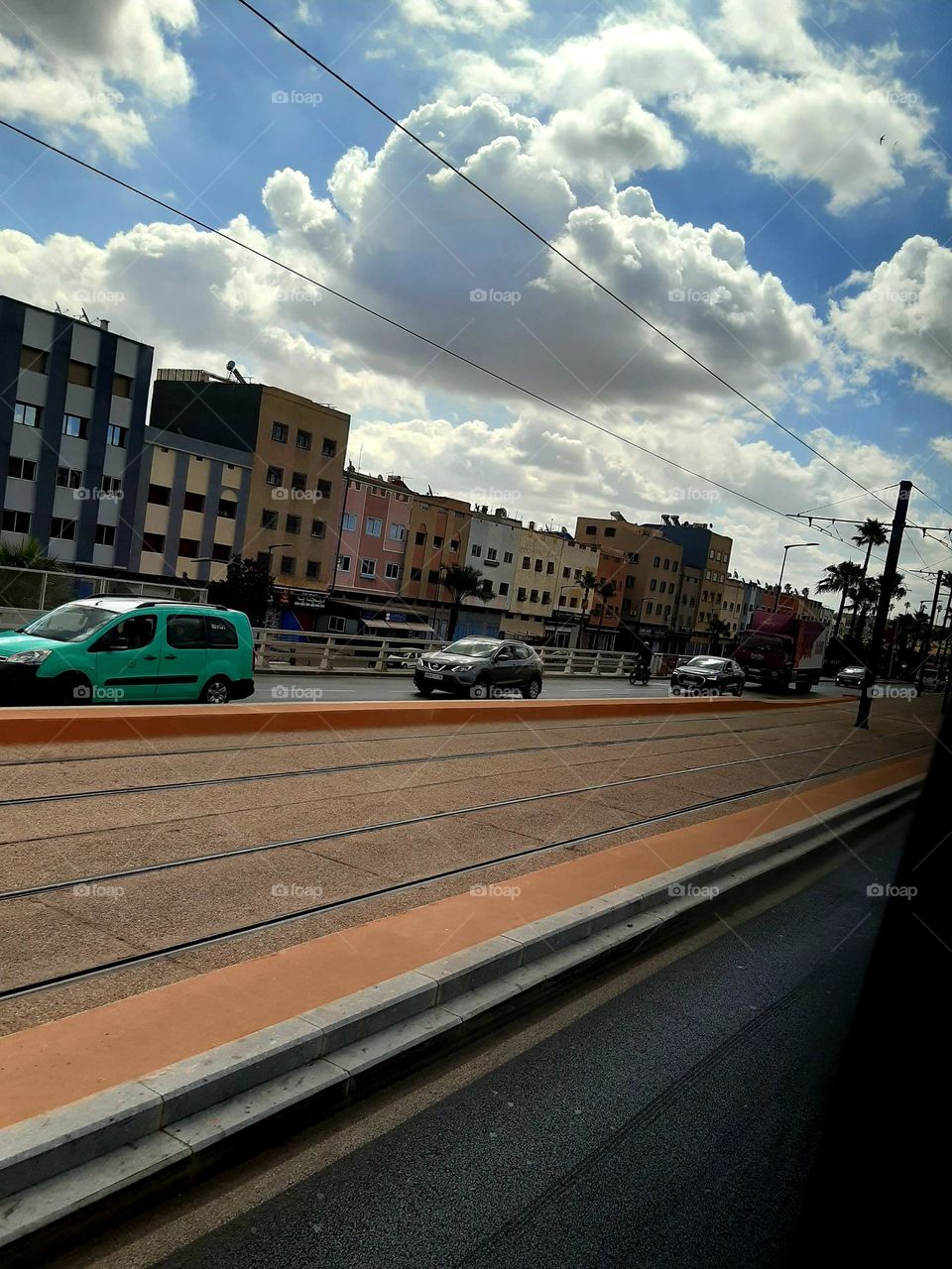 A busy street in Casablanca on January 1, 2025, with cars and pedestrians alongside railway tracks. A train passes by, highlighting the city's dynamic blend of modern life and transportation.