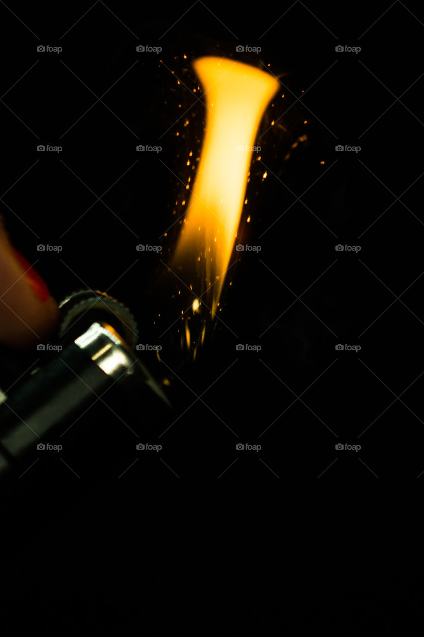 A person has lighters in his hands and he lights it through a flint wheel, the lighter ignites, sparks and fire appear, close-up on a black background.