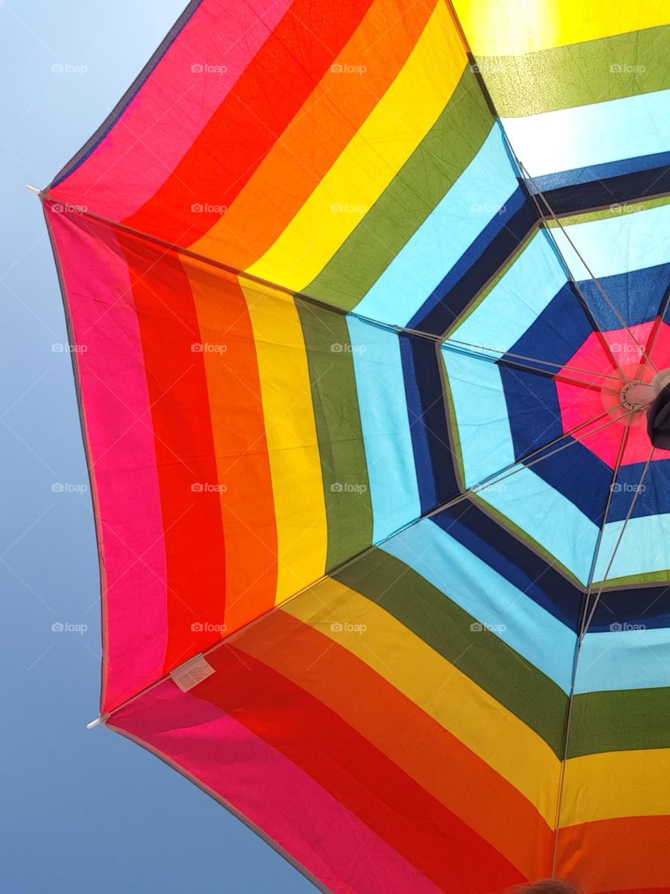 rainbow colored sun umbrella with blue sky on a hot summer day close up picture