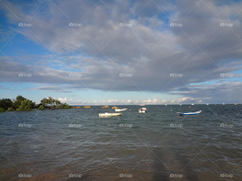 Boats at the sea close to the beach in a cloudy blue sky