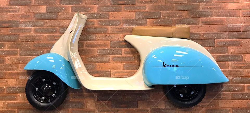 Scooter blue and white hanging on brick wall, decorative.