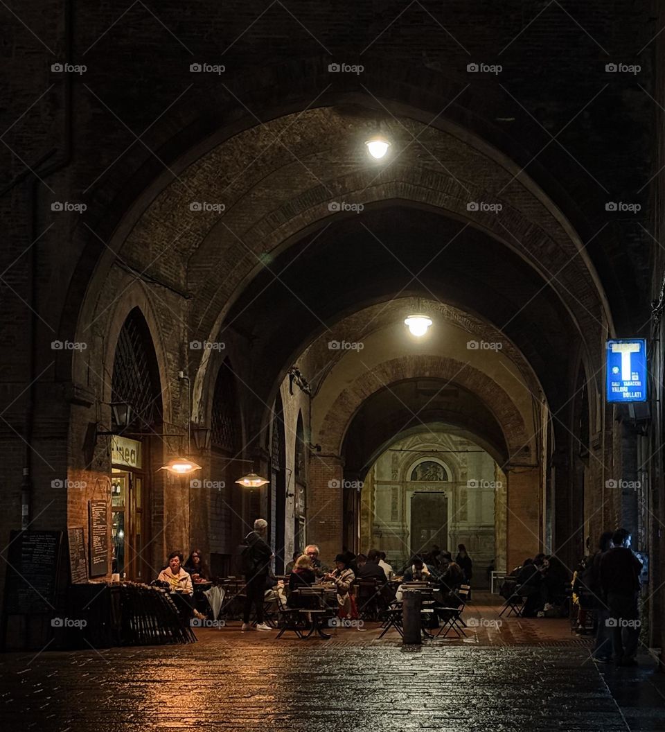 Rainy evening in Bologna, Italy. People sitting outside. Nice old arch, grate monumental dark arch, dark architecture 