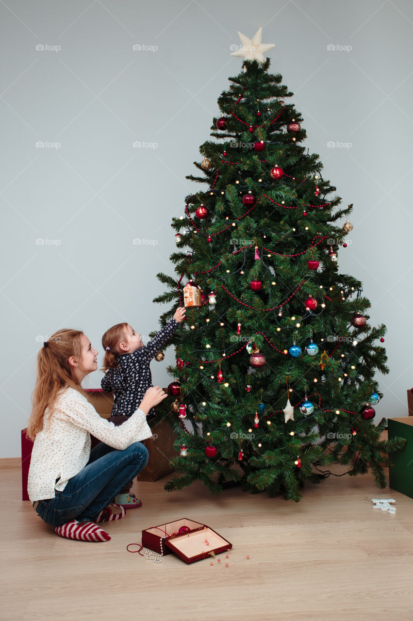 Young girl and her little sister decorating Christmas tree at home