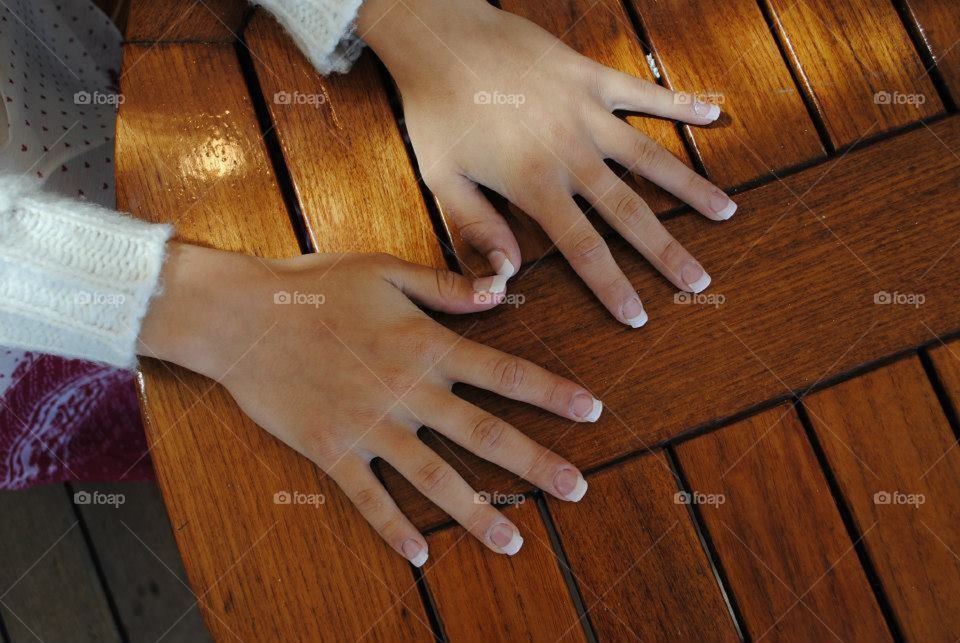 Manicured hands splayed out on a dark wooden table. 
