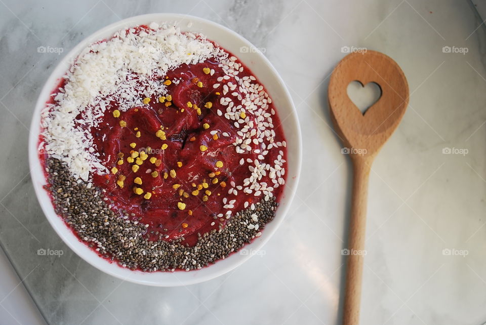 Berry smoothie bowl with bee pollen chia seeds and coconut with wooden spoon 