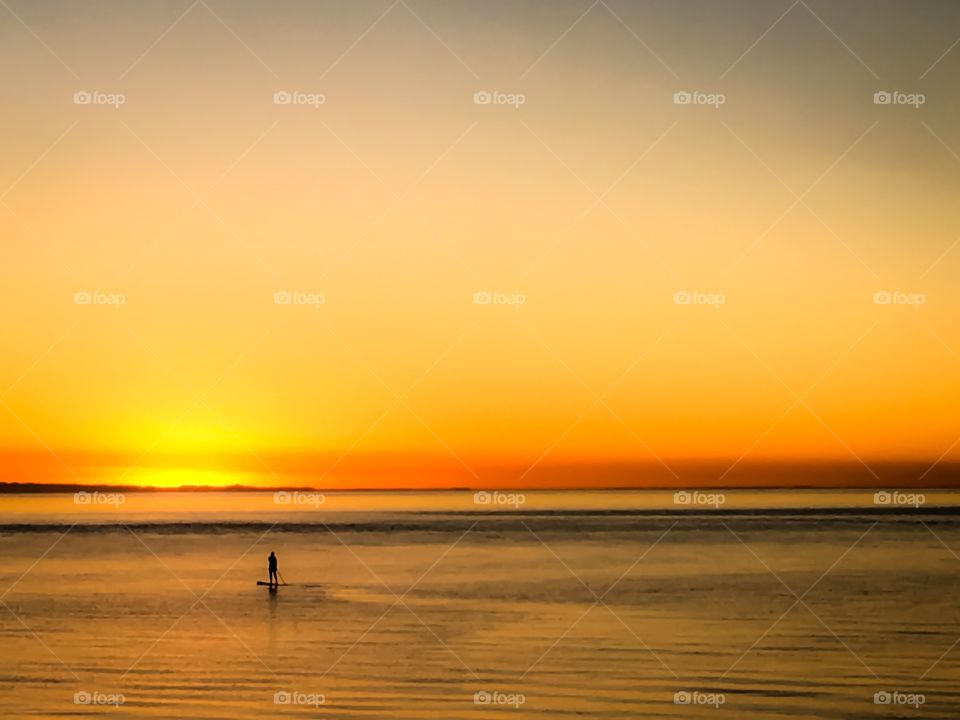 Paddle boarder on the ocean at dawn sunrise silhouette  