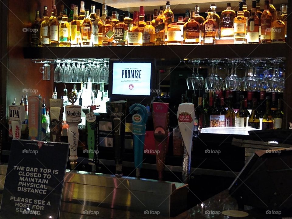 beer tap and liquor display at a closed bar with a social distance sign