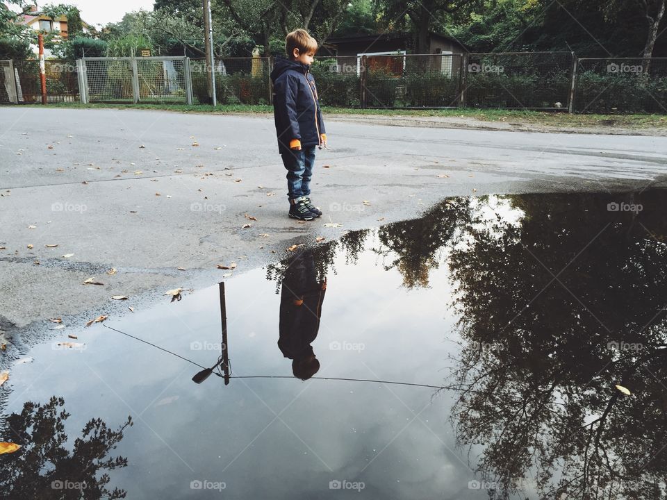 Child standing at puddle. Boy standing in front of huge puddle with sky reflections