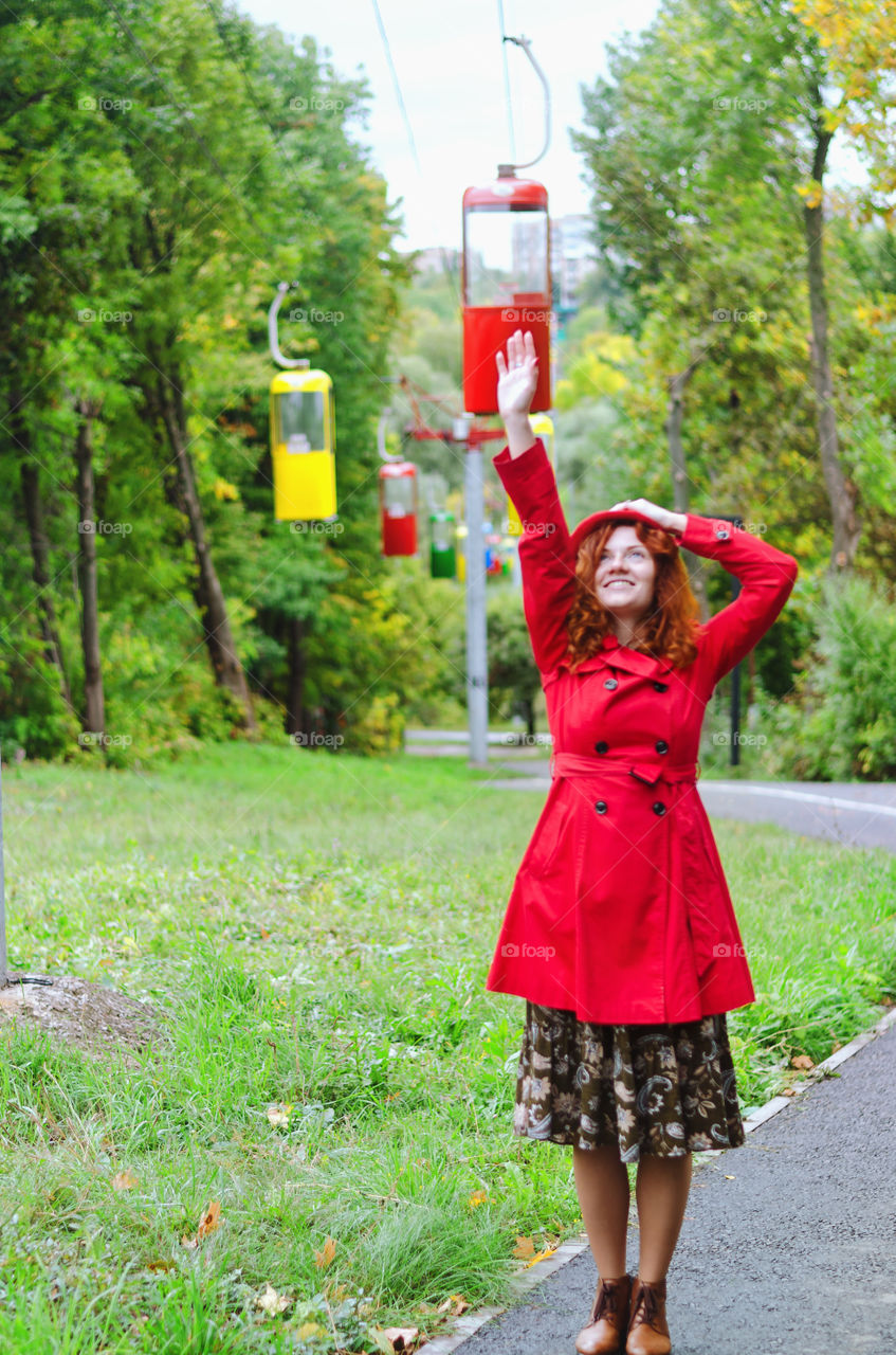 Young happy woman with red hair, freckles in a red beret and a coat walking in autumn park. Fall cold season