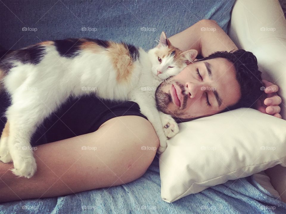 Cat lying on man sleeping on sofa