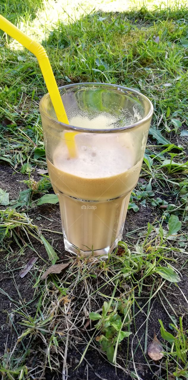 An ice cold coffee drink in the glass with a yellow straw.