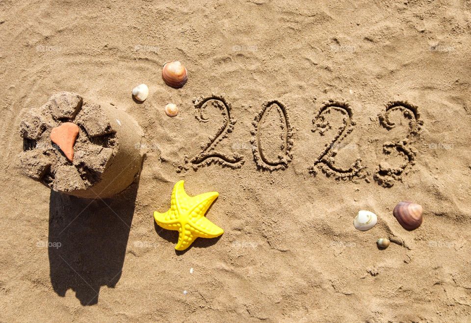 Sand castle with shells and the inscription 2023 on the seashore on a summer sunny day, flat lay close-up.