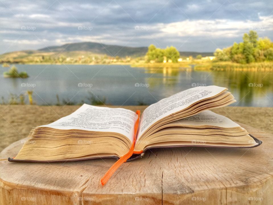Open book sitting on wooden table with view of lake in front 