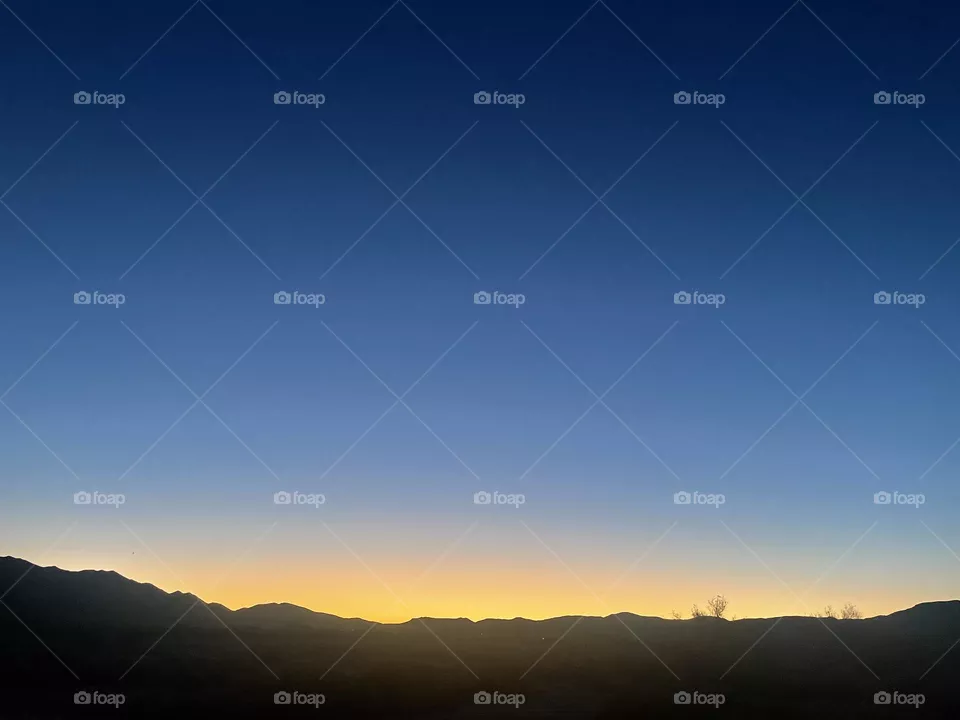 A yellow sunset with mountains and the night sky above.