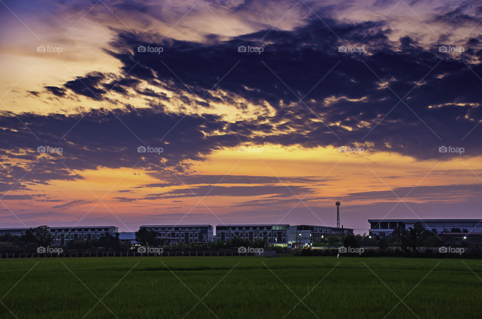 Beautiful light of Sunset with clouds in the sky reflection behind the building and paddy fields.