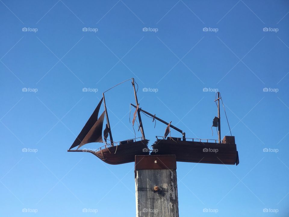 Rusted metal sculpture atop wharf piling, of shipwreck