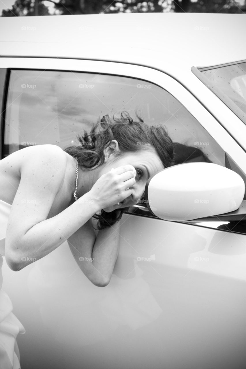 Woman looking at car side mirror wiping her eyes