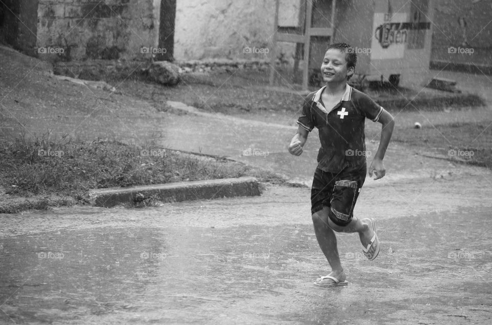 A Asian boy running on road in rain