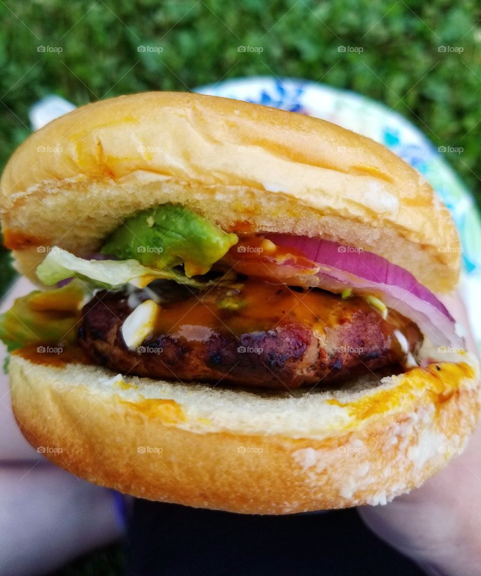 Close up of a grilled turkey burger on a bun with onion avocado and sauces at a summer cookout