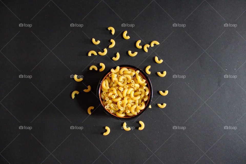 Top view of black background with italian raw pasta horns in a bowl.