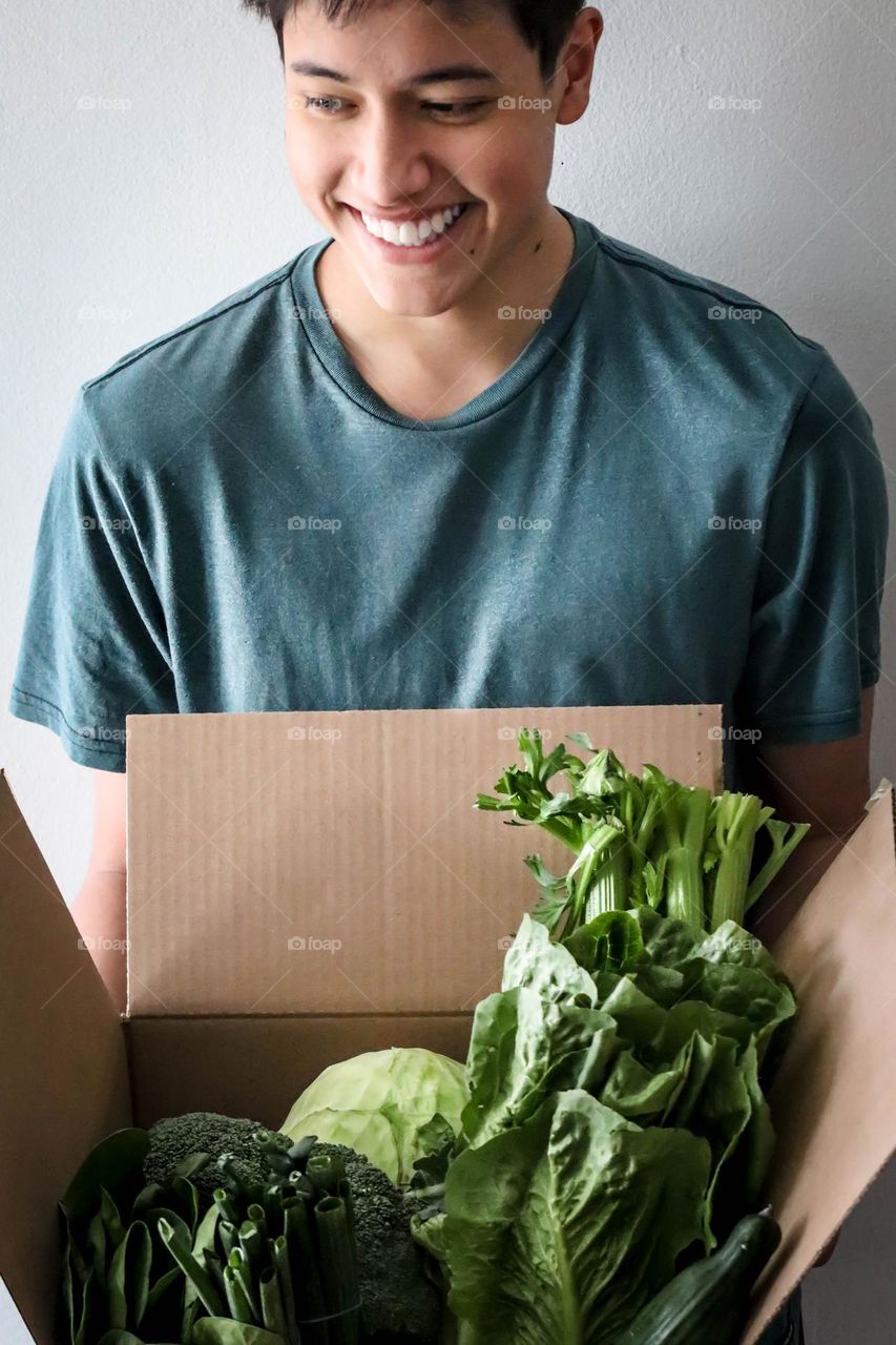 Happy handsome young man with a box of green vegetables