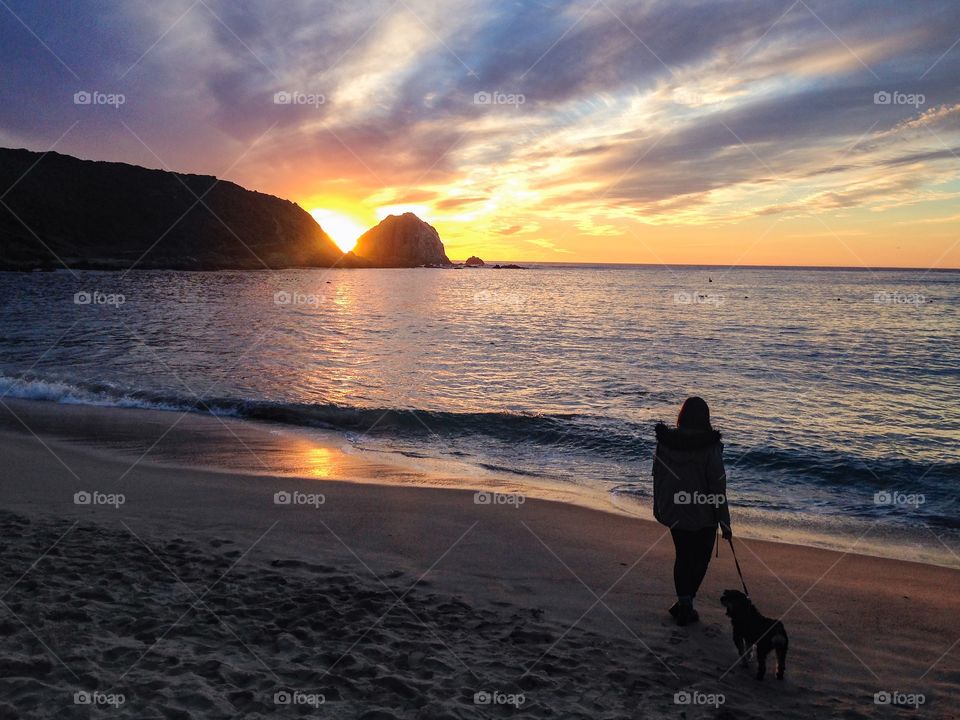 Woman and her dog walking at the beach at a beautiful sunset 