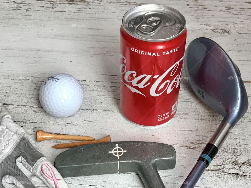 A can of Coca Cola and golf equipment on a rustic white background 