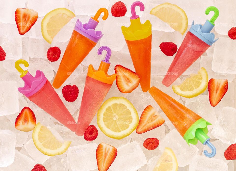 Colourful fruity ice lollies and fruit pieces on a bed of ice. 