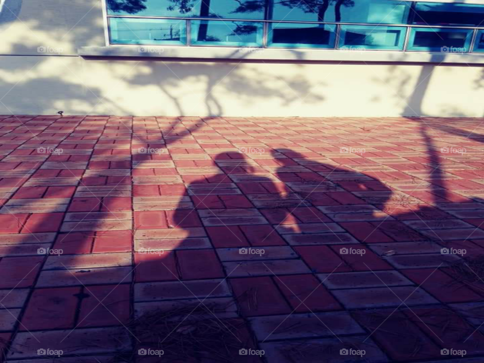 a shadow of a mother who's  sitting  while her daughter is standing beside her while listening  to the music from the fone.