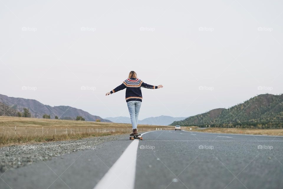 Young woman on skateboard on road against beautiful mountain landscape, Chuysky tract, Altai