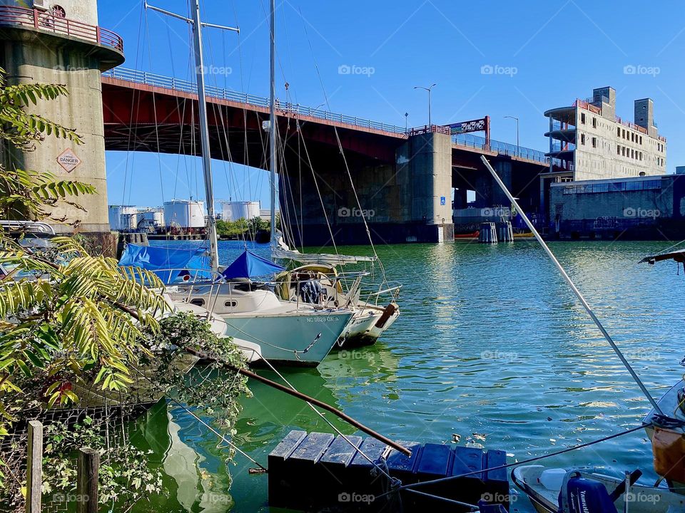 This is the “Pulaski Bridge” at “Newtown Creek” seen from the LIC shore. Two sailboats can also be seen on the waters of the “East River” on a lovely Indian summer day in early October 2023. Hypnotic Productions