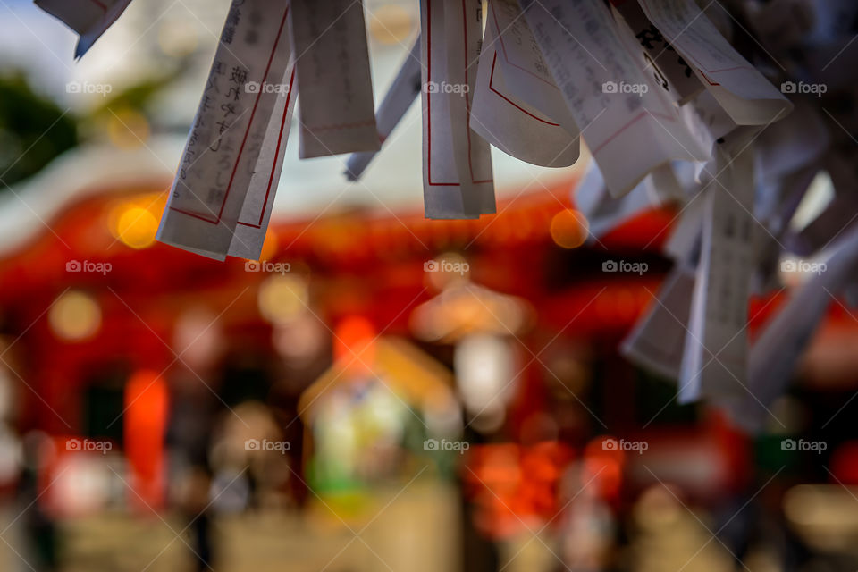 Paper charms tied close together, with a Japanese Shrine defocussed in the background.