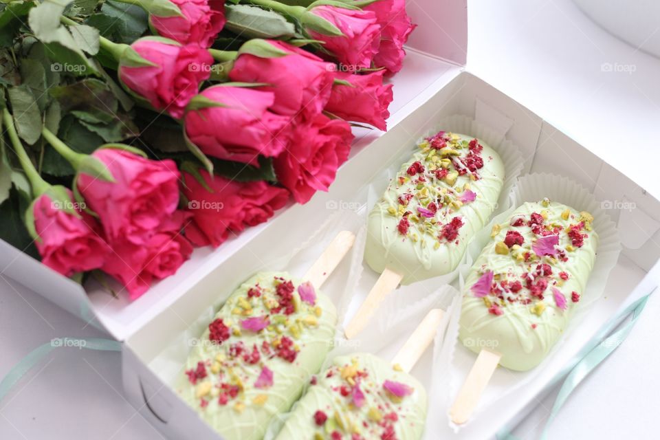 four Popsicle cakes in a white box and a bouquet of bright pink roses