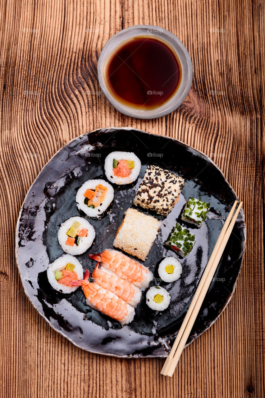 Sushi set on pottery plate with chopsticks and soy sauce in bowl on old wooden table from above